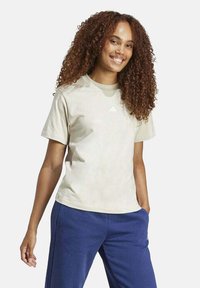 Camisa beige de manga corta con cuello redondo y logo blanco en el pecho, combinada con pantalones azul oscuro. Tela de algodón texturizada.
