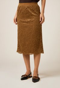 Brun spets midi kjol med en figursydd midja, intrikata blommönster och en slät textur, kombinerad med svarta lägenheter med en rosettdetalj.