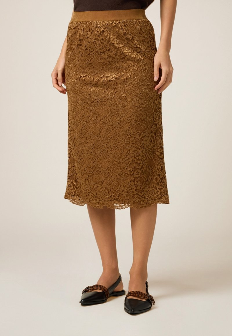 Brun spets midi kjol med en figursydd midja, intrikata blommönster och en slät textur, kombinerad med svarta lägenheter med en rosettdetalj.