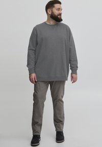 Sudadera gris de manga larga, con cuello redondo; combinada con pantalones gris claros y zapatos negros. El conjunto presenta un ajuste relajado.