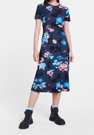 Mujer con un vestido midi azul marino con estampados florales en rosa y azul, combinado con botines negros y calcetines azul claro.