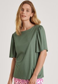 Groen mouwloos topje met een bootnek, voorzien van verzamelde schouderaccenten en een gladde textuur. Gecombineerd met gestreepte roze onderstukken.
