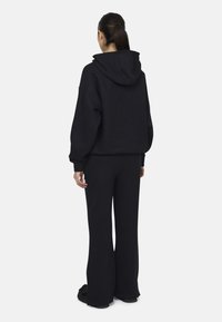 Felpa nera in cotone con una vestibilità comoda, dotata di cappuccio con coulisse e polsini a coste, abbinata a pantaloni larghi coordinati.