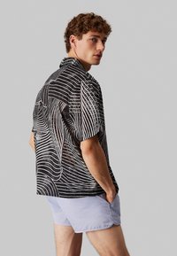 Maglietta nera con motivi a linee ondulate bianchi, maniche corte e colletto. Abbinata a pantaloni corti blu chiaro. Tessuto dalla consistenza liscia.
