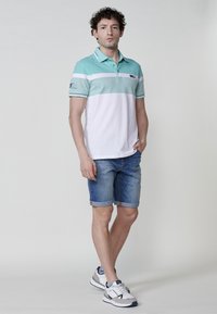 Turquoise és fehér csíkos pólóing, gallérral és rövid ujjakkal. Farmer rövidnadrággal és sportcipőkkel viselve.