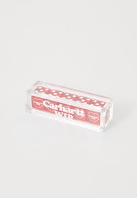 Selge akrüülkarp, mis sisaldab punaseid täringuid valgete punktidega, mille küljele on valgest värvist kirjutatud "Carhartt WIP". Karbil on siledad servad ja ristkülikukujuline kuju.