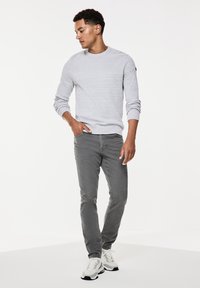 Jasnoszary sweter o jedwabistej teksturze z okrągłym dekoltem, w połączeniu z szarymi spodniami typu slim fit oraz białymi trampkami z czarnymi i zielonymi akcentami.