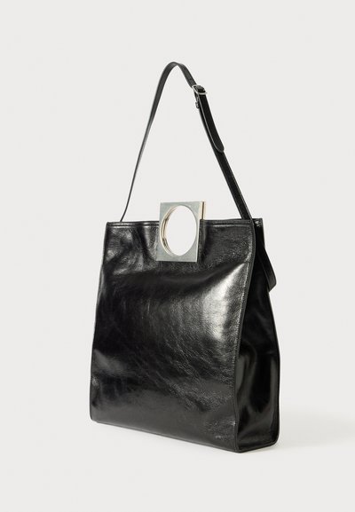 Black leather handbag with a structured design. Features a circular metal accent on a square panel. Adjustable shoulder strap included.