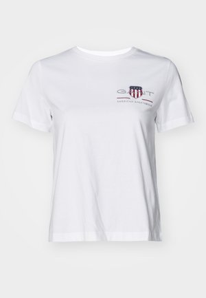 T-shirt bianco in cotone con maniche corte, colletto rotondo e un logo ricamato rosso e blu sul lato sinistro. Tessuto liscio, vestibilità morbida.