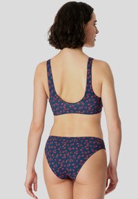 Navy bikini sarjana dengan corak bunga merah. Bahagian atasnya mempunyai tali lebar dan belakang yang berbentuk sudu; bahagian bawahnya mempunyai reka bentuk kaki tinggi.