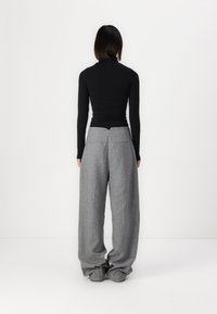 Crna turtleneck majica dugih rukava s uskim krojem, uparen s labavim, visokim sivim hlačama koje imaju stražnje džepove i teksturiranu tkaninu.
