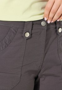 Pantaloni grigi scuri con due bottoni circolari argentati in vita, che presentano cuciture a contrasto e tasche sul davanti. Tessuto dalla texture liscia.