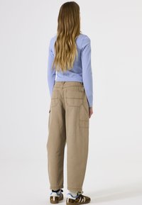 Lichtblauw langemouwen shirt, gecombineerd met losse beige cargobroek met opgestikte zakken en een gestructureerde afwerking, gedragen met gemusterde sneakers.
