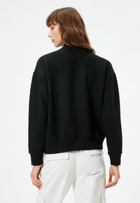Czarny oversize pulower wykonany z teksturowanej tkaniny z okrągłym dekoltem i ściągaczami u rękawów, prezentujący subtelny wzór.