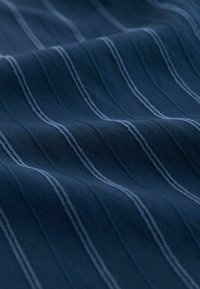 Tissu bleu foncé avec des fines rayures blanches verticales espacées de manière régulière, présenté avec de doux plis et des détails de texture raffinés.