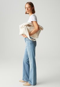 Borsa a spalla in tela di colore bianco sporco, ampia con manici resistenti, abbinata a jeans a campana azzurri e ballerine beige. Design semplice e funzionale.
