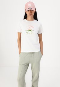 Witte T-shirt met een kleurrijke grafische print van een ster en merknaam, gecombineerd met lichtgroene joggingbroek met een trekkoord in de taille.