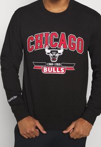 Maglietta a maniche lunghe nera con la scritta "CHICAGO BULLS" in rosso e bianco, con un'immagine di un toro e "1968-1969" sottostante. Tessuto morbido in cotone.