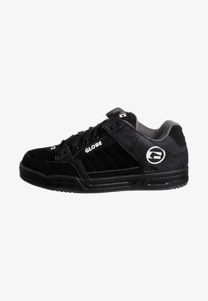 Svarte skate-sko med overdel i semsket skinn og mesh, polstret krage, teksturerte detaljer og en fremtredende logo på siden. Flate snøringer.