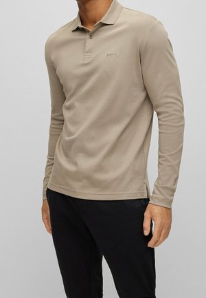 Beżowa polo koszulka z długim rękawem, wykonana z miękkiego materiału, z kołnierzykiem, trzema guzikami na przodzie i małym haftowanym logo na piersi.