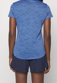 Haut de sport bleu avec un motif texturé subtil, manches courtes et ourlet arrondi, associé à un short bleu marine.