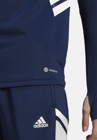 Marine blauwe sporttop gemaakt van ademend materiaal. Bevat witte strepen en een klein logo, heeft een slim-fit ontwerp en gestructureerde mouwen.
