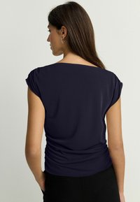 Top azul marino de tejido suave, con mangas cortas enrolladas y detalle fruncido en la parte posterior, que complementa una silueta ajustada.