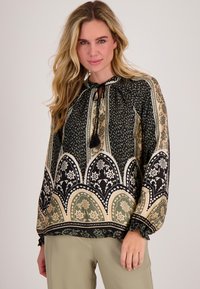 Blouse met een hoge halslijn, voorzien van zwarte en groene bloemenpatronen, elastische manchetten en een trekkoord met kwastjes.