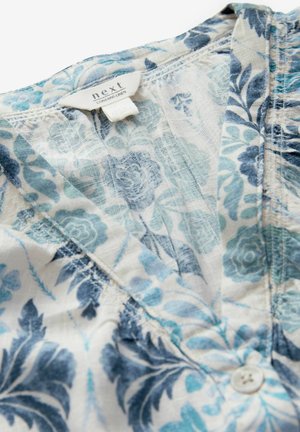 Linane särk, millel on lillemuster sinise ja türkiissinise värviga heledal taustal. Nööbiga kinnitamine ja silt nähtavad kaelaosa juures.