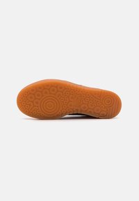 Schuhsohle aus orangefarbenem Gummi mit kreisförmigen und wellenähnlichen Mustern, beschriftet mit "Puma" in der Nähe des Fußgewölbes.