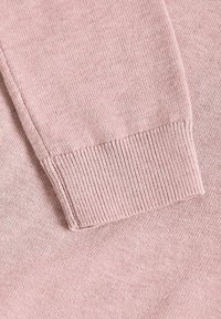 Gros plan sur une manche de pull rose tricoté montrant un poignet côtelé et une texture fine de tricot sur un tissu doux.