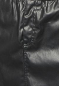 Pantalons en cuir noir avec une texture brillante, dotés d'une poche latérale et d'une taille froncée, présentant des coutures lisses et une coupe ajustée.