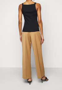Black sleeveless top with a square neckline paired with beige wide-leg trousers. Smooth fabric, minimal seams, with open-toe black heels.