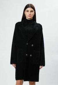 Cappotto nero doppiopetto realizzato in materiale peloso, con colletto a revers, due tasche frontali e bottoni decorativi.
