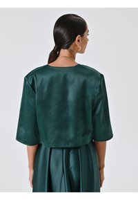 Top corto in satin verde scuro con maniche ampie e scollatura rotonda, abbinato a un pantalone in satin dello stesso colore. Texture liscia e finitura lucida.