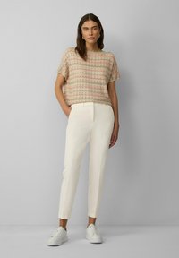 Gebreid top met korte mouwen in lichtbeige met multicolor zigzagpatronen, gecombineerd met slanke witte broeken en witte sneakers.