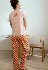 Helles rosa Baumwoll-T-Shirt mit einem kleinen orangefarbenen karierten Design auf der Rückseite, kombiniert mit orange-weißen karierten Hosen.
