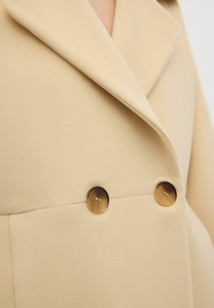 Beige wool blend coat featuring a notched collar and two round, faux horn buttons at the front, with smooth texture and tailored design.