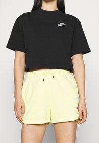 Black cropped t-shirt with white Nike logo, paired with light yellow shorts featuring an adjustable drawstring and small purple Nike logo.