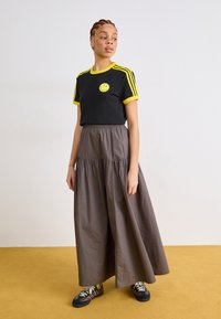 Black t-shirt with yellow accents and smiley graphic, paired with a long, flowing gray skirt. Model wears multicolored sneakers.