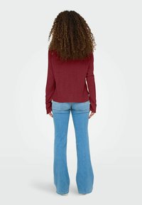 Burgunderfarbener Langarmoberteil mit einem lockeren Schnitt, kombiniert mit hellblauen Schlagjeans. Der Stoff scheint weich mit einer glatten Textur zu sein.