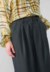 Button-up-Hemd in gelb-braunem Karomuster, kombiniert mit dunkelgrauen, gep тарабынан versehenen Hosen mit vertikalen Streifen und maßgeschneiderter Passform.