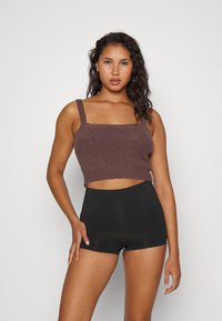 Brun strikket croppet topp med brede stropper og en teksturert overflate, sammen med høyt liv svarte shorts som viser en tettsittende design.