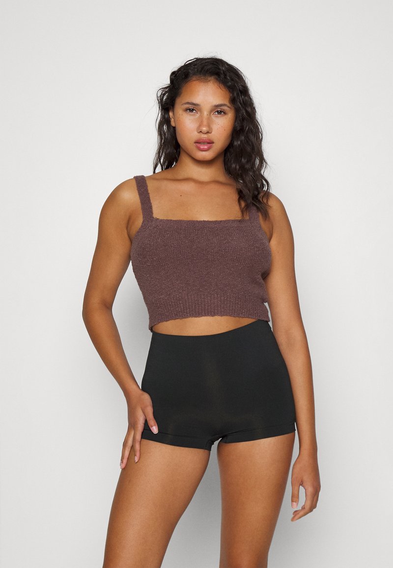 Brun strikket croppet topp med brede stropper og en teksturert overflate, sammen med høyt liv svarte shorts som viser en tettsittende design.