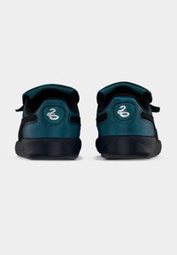 Sneakers with a teal suede upper and black mesh accents, featuring a Velcro strap and rubber outsole, detailed with a silver logo on the heel.