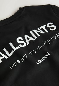 Svart tyg med vit text "ALLSAINTS", japanska tecken och "LONDON" tryckt på det.