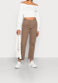 Vit off-shoulder topp med smockad byst, bruna raka byxor och vita sneakers. Tillbehör: vit väska med nitar på remmen.