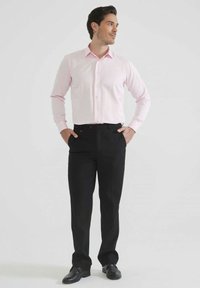 Chemise rose clair à manches longues avec boutons, associée à un pantalon noir. La chemise a un col classique et des boutons sur le devant.