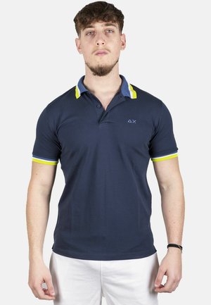 Polo shirt blu navy realizzato in cotone con colletto blu e dettagli giallo neon sul colletto e sulle maniche, dotato di un piccolo logo sul petto.