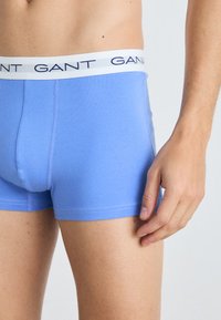 Blaue Baumwoll-Boxershorts mit einem weißen Bund, auf dem das Logo "GANT" aufgedruckt ist. Glatter Stoff, enganliegendes Design und mittellange Beine.